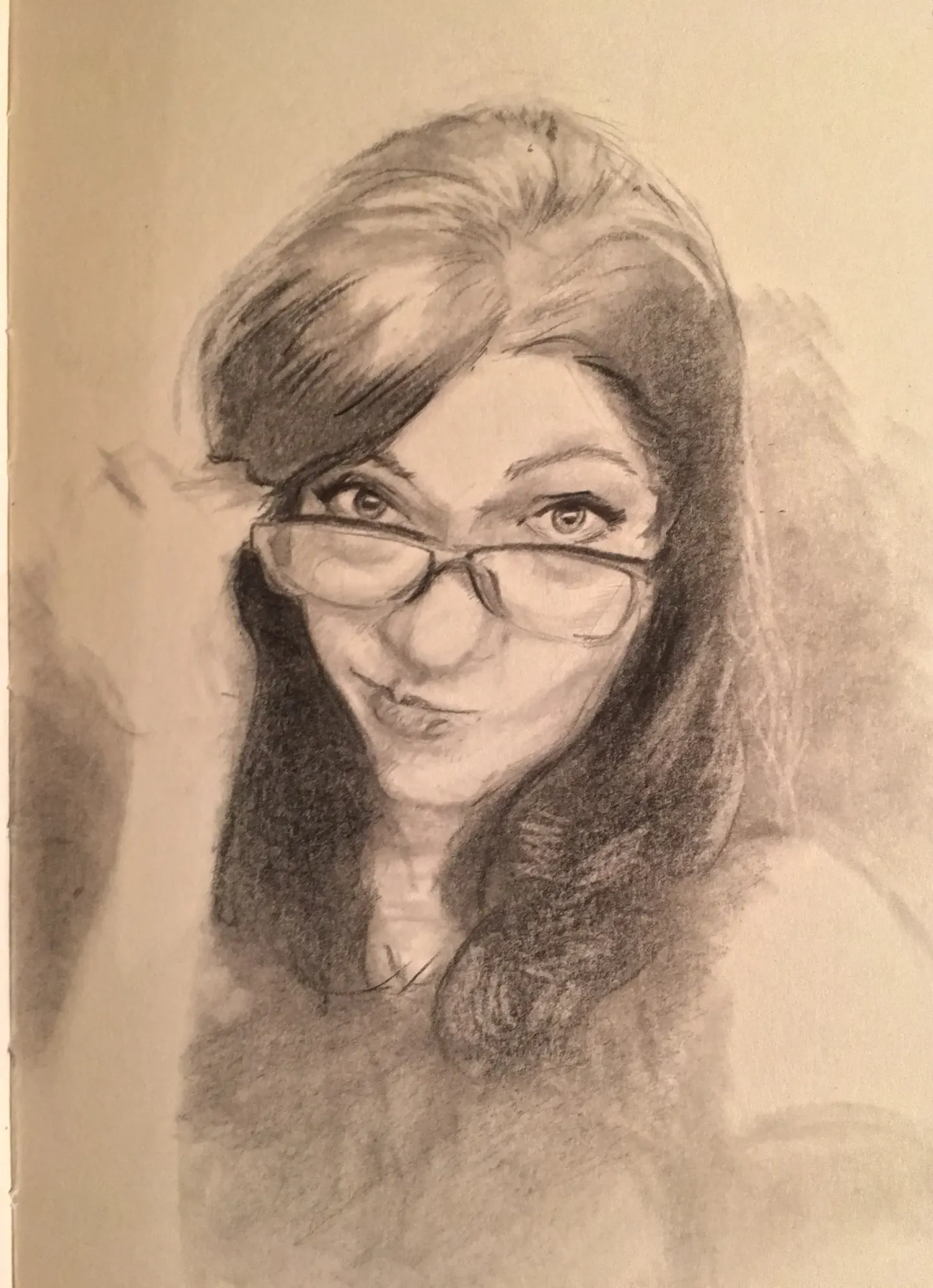 Unfinished pencil portrait of Andrea in a sketchbook. She looks over her glasses with a playful, puckered expression; long dark hair frames her face, and the lower half is still loose sketch lines.